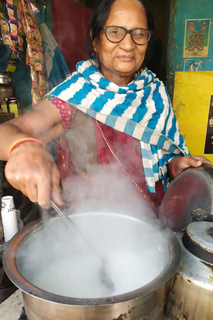 Indiase vrouw roert in een pan met verse melk dat gebruikt wordt voor de thee